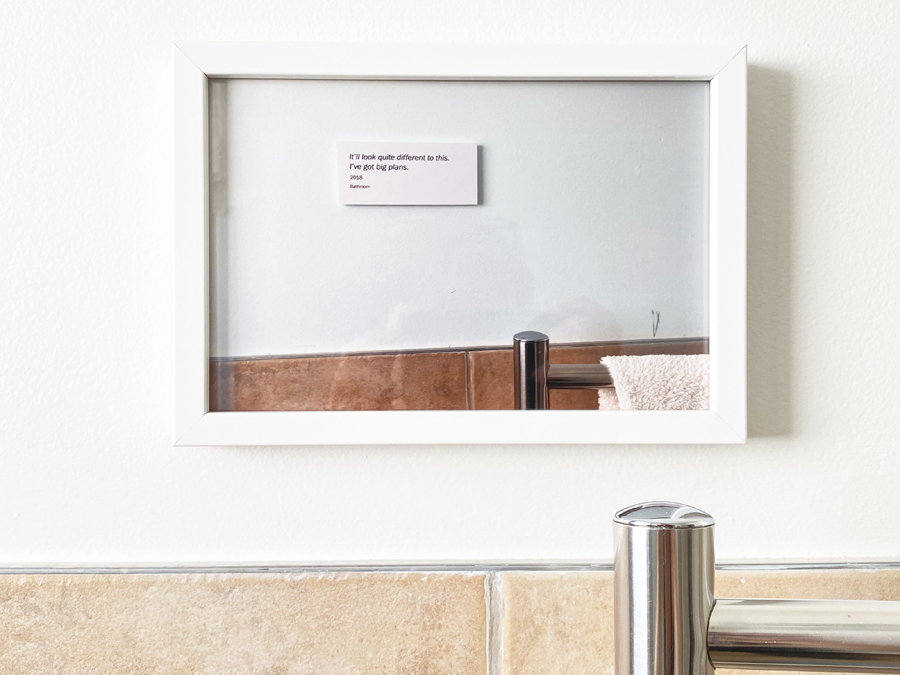 Image of a framed photograph on a wall. The photograph features the same section of wall and a exhibition label which says 